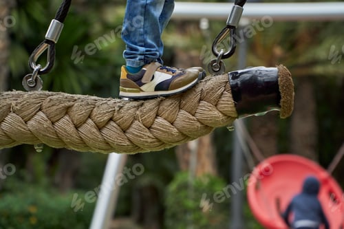 Preview: Unrecognizable kid swinging from hanging rope at the park