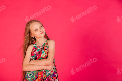 Preview: Dreaming little girl in colorful t-shirt posing arms crossed at pink background