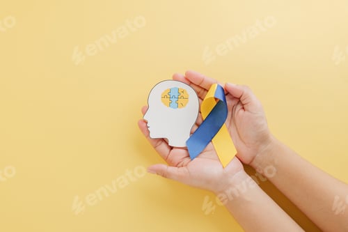 Preview: Hands hold a head with puzzle pieces and a ribbon for Down Syndrome.