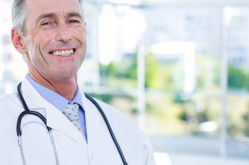 Preview: Senior male doctor standing beside window in clinic wearing white coat with stethoscope, copy space