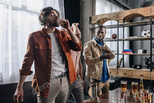 Preview: young multiethnic male friends drinking tequila while partying together indoors