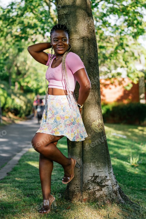 Preview: A woman in a pink shirt and floral skirt is posing in front of a tree