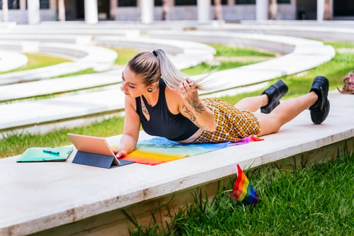Preview: Back to School. Modern student with tattoos studies lying on an LGTBI flag