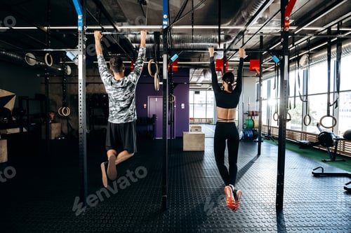 Preview: Slender girl and athletic man dressed in sports clothes are pulling up on the bar in the gym