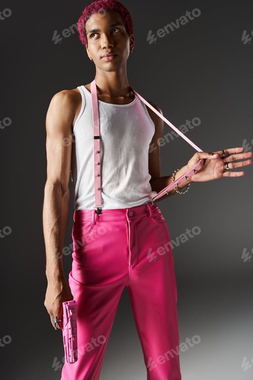Preview: good looking man with curly pink hair with hand on suspenders holding toy gun and looking away