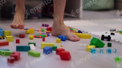 Preview: barefoot man walks among the scattered toys. Foot stepping on children's toys.