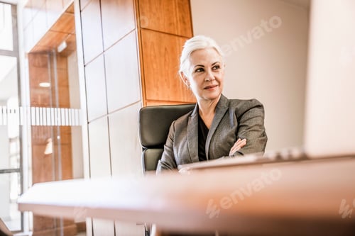 Preview: Businesswoman sitting at desk arms crossed looking away