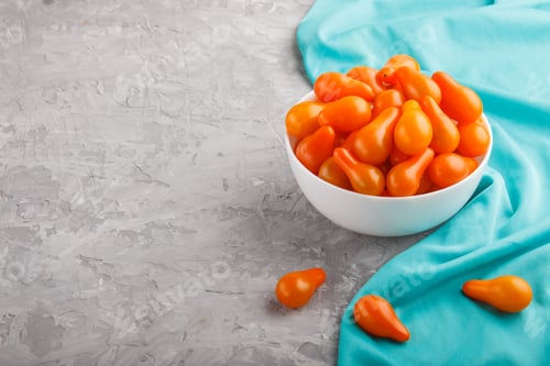 Preview: Fresh orange grape tomatoes in white ceramic bowl on gray concrete background with blue textile