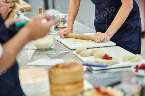 Preview: focused view of cropped mature woman using rolling pin next to blurred african american colleague