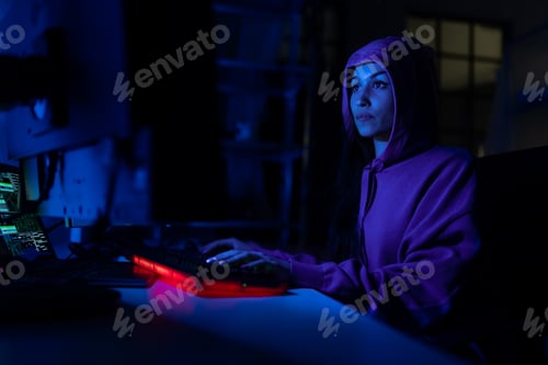 Preview: Young woman hacker by computer in the dark room at night, cyberwar concept.