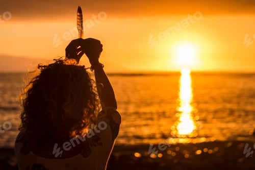 Preview: Freedom and meditation concept image with woman taking a feather like life during a sunset