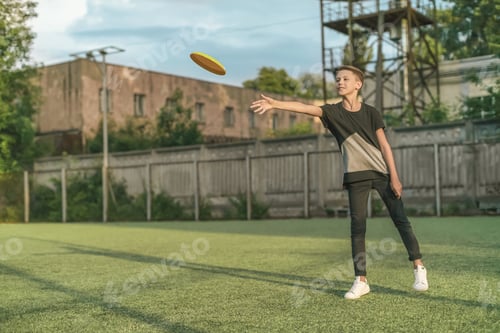 Preview: full length view of cute smiling boy throwing flying disk on green lawn