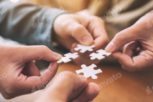 Preview: Closeup image of many people hands holding and putting a piece of white jigsaw puzzle together