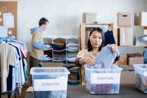 Preview: Asian woman choosing clothes from donation boxes