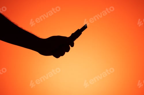 Preview: Hand holding scalpel on orange background. Silhouette photography