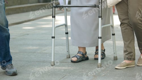 Preview: Senior woman walking with metal walker outdoors.