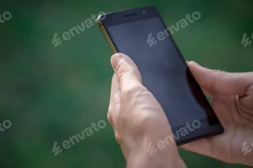 Preview: hand hold black smart phone, cell phone, mobile over blurred image of green forest background