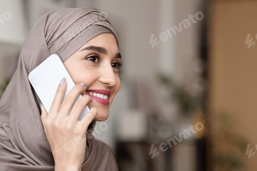 Preview: Portrait of modern muslim girl in hijab talking on cellphone indoors