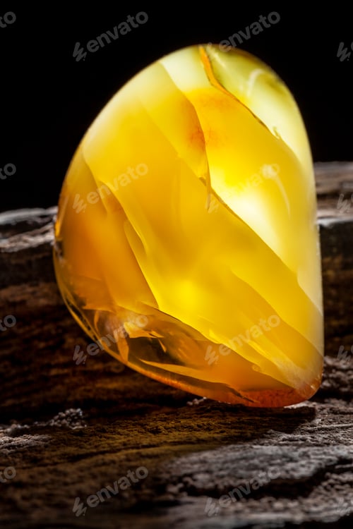 Preview: Natural amber. A piece of yellow opaque natural amber on large piece of dark stoned wood