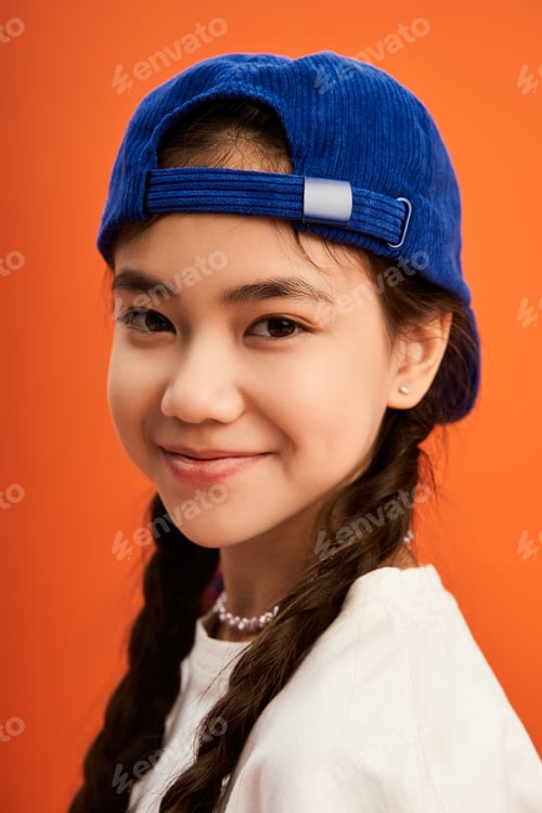 Preview: Stylish Asian teenager poses confidently in vibrant studio setting with orange backdrop
