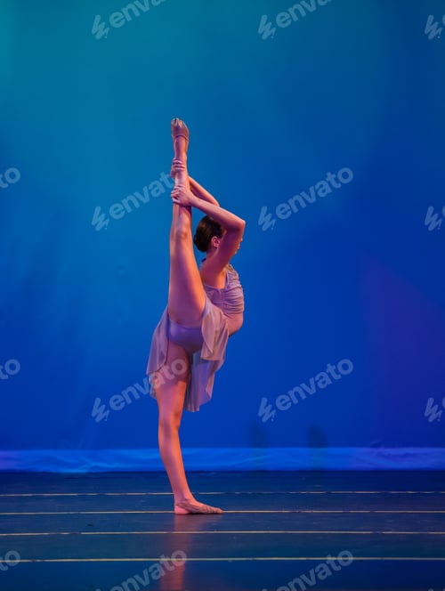 Preview: Vertical shot of a ballerina standing in a high kick pose on a stage with blue background