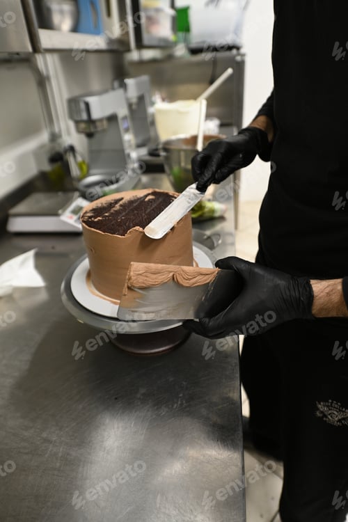 Preview: pastry chef smooth level sculpt cream on frosted layered dark chocolate cake in professional kitchen