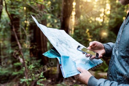 Preview: Mid section of man holding map and using smart phone