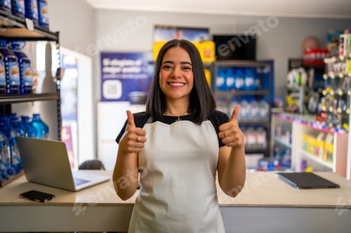 Preview: Smiling woman wearing apron standing at counter giving two thumbs up gesture