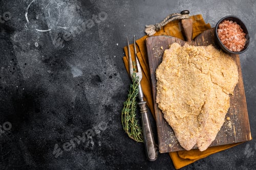 Preview: Wiener breaded raw pork Schnitzel, meat steak on a wooden board. black background. top view