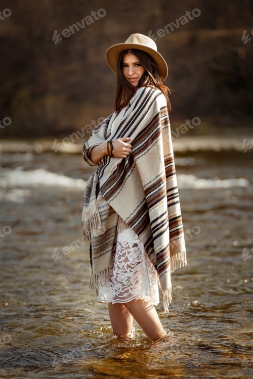 Preview: beautiful woman traveler wearing hat and poncho standing in water of river