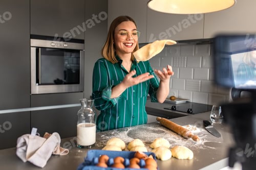Preview: Young woman recording video blog with smart phone at home in kitchen making croissants.