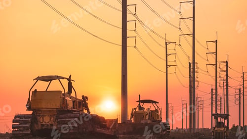 Preview: Silhouette of 3 bulldozer tractors parking on country road with electric poles against sunset sky