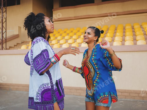 Preview: Portrait of young African American women have conversation outdoors on stadium.Colorful ethnic cloth