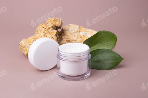 Preview: Open cosmetics container with white cream and glossy green leafs on background,eco friendly concept.