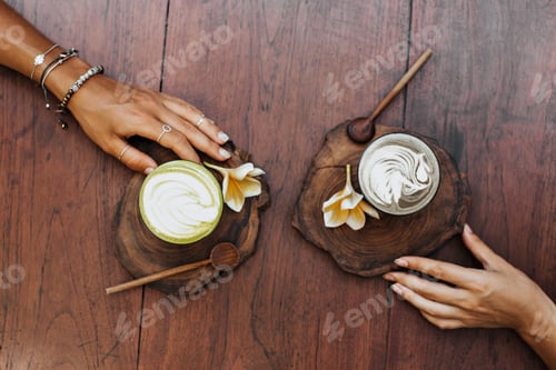Preview: Flat-lay. Photo of tanned female hands on wooden table. Snapshot of cup of matcha tea with milk and