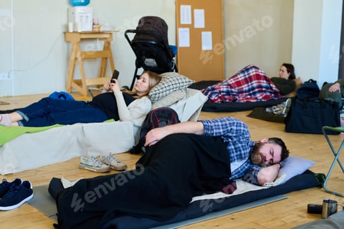 Preview: Young tired man sleeping under blanket while lying on mattress on the floor