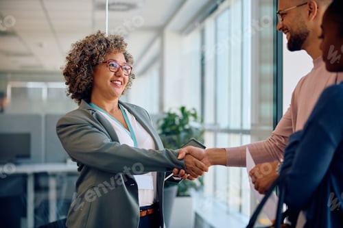 Preview: Happy insurance agent shaking hands with young couple as they meet in the office.