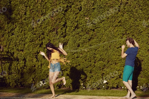 Preview: Couple having fun pour each other with garden hose