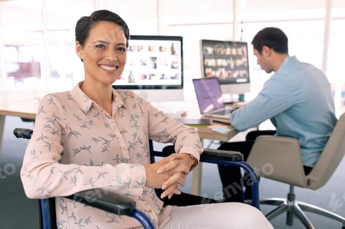 Preview: Happy disabled mixed race female graphic designer in wheelchair looking at camera in a modern office