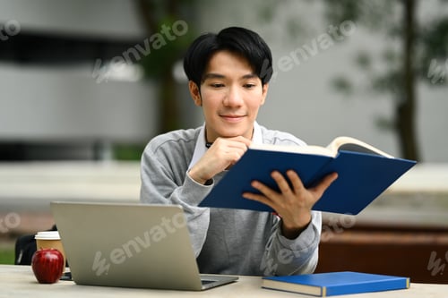 Preview: Smiling man reading book or studying for exam, doing homework remotely.