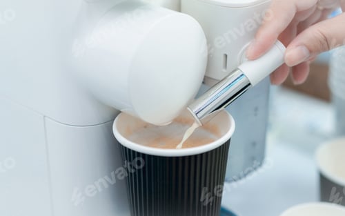 Preview: Woman making a cup of hot coffee with capsule coffee machine. Woman hand holding frothed milk