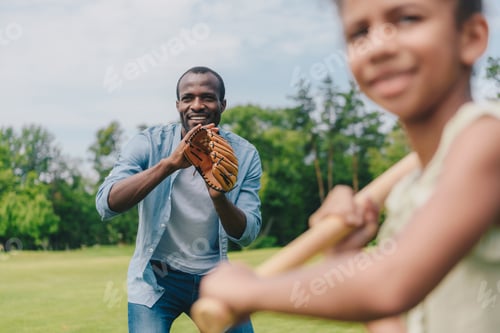 Preview: selective focus of smiling african american young man and little daughter playing baseball together