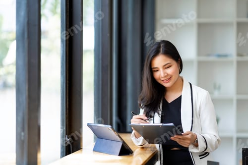Preview: An Asian businesswoman wipes her to-do list at her desk in a modern office.