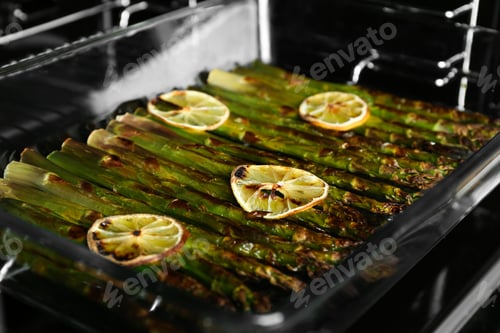 Preview: Cooked asparagus with lemon slices in glass baking dish on oven rack, closeup