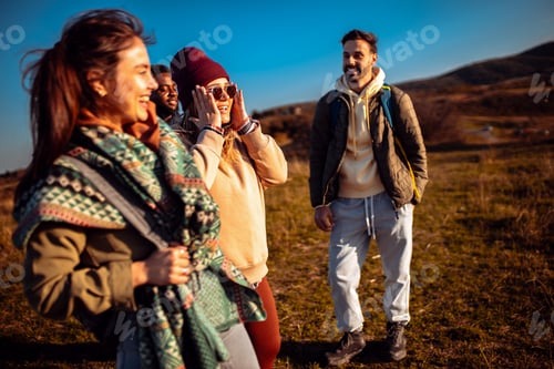 Preview: Smiling group of friends having fun while hiking together on hill at sunset.