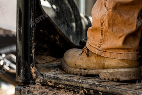 Preview: Close-up shot of brown leather boot of a construction worker sitting on an aged dirty tractor