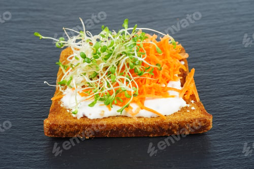 Preview: Green alfalfa sprouts, and grated carrots on toasted slices of wholegrain bread on black stone