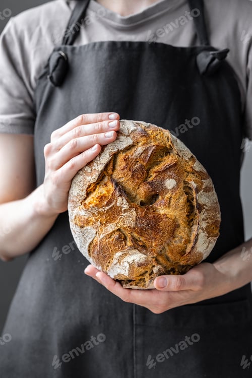 Preview: caucasian woman holding fresh bread from the oven, baking homemade bread