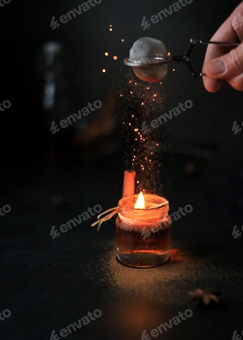 Preview: An alcoholic cocktail lit by fire and sparks, sprinkled with ground cinnamon, on a dark background