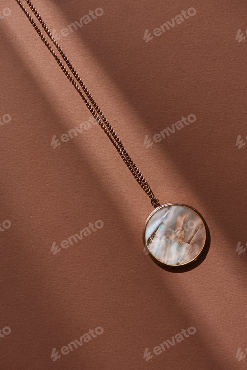 Preview: top view of beautiful round locket with marble on brown surface with sunlight